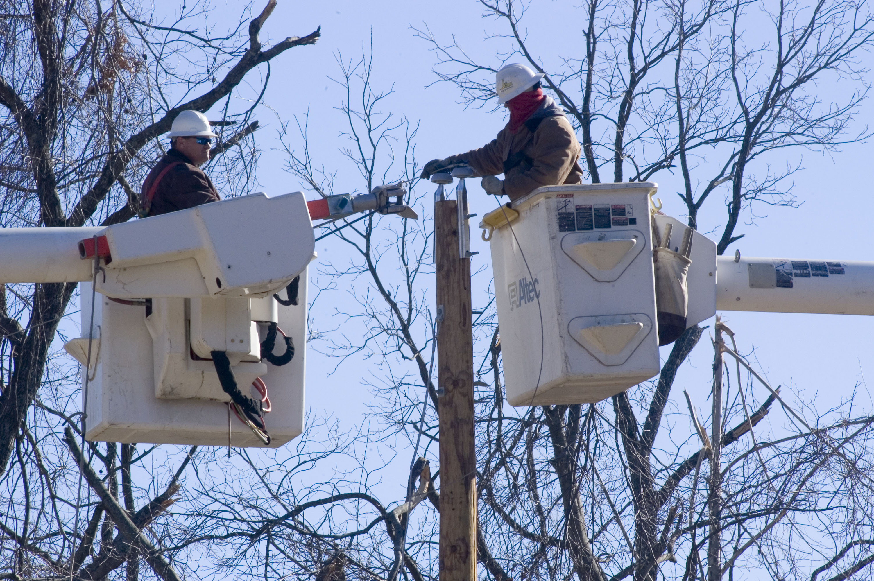 Two men in bucket lifts working on power line